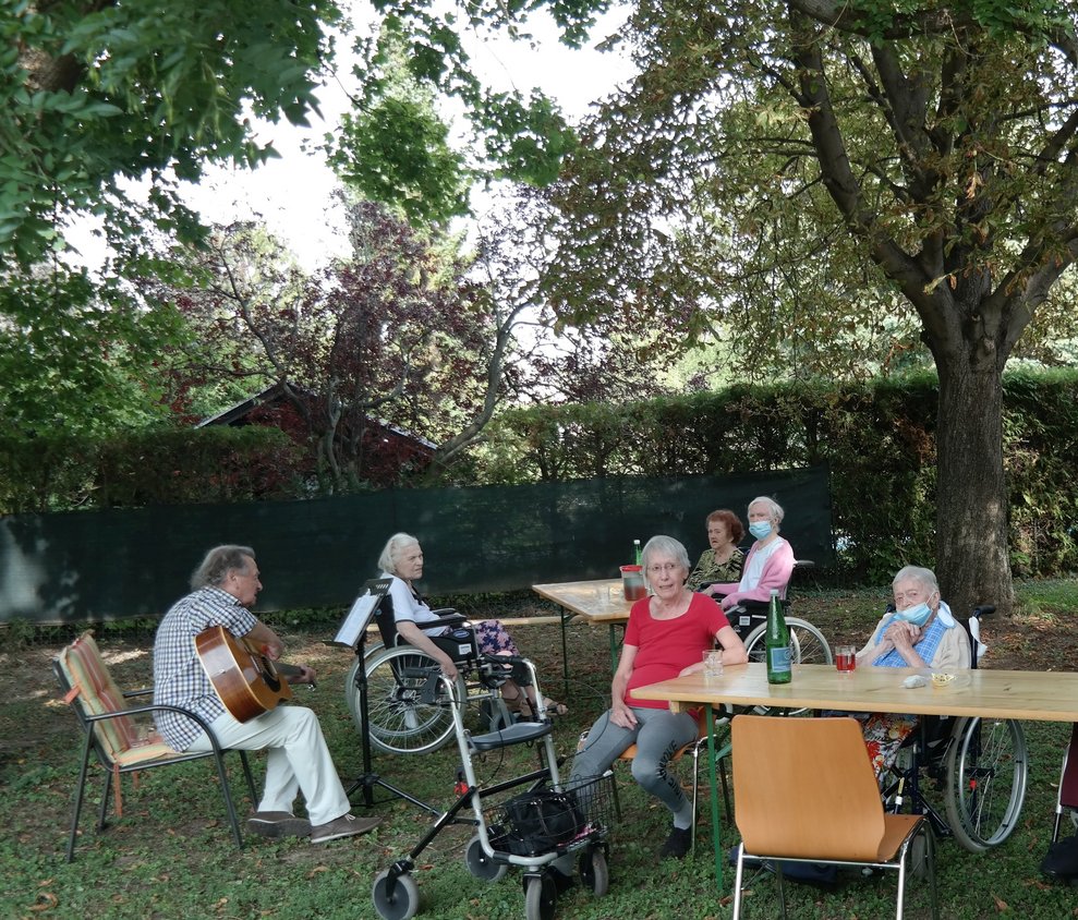 BewohnerInnen sitzen draußen und einer singt.