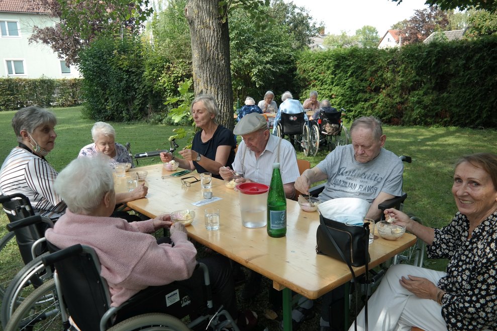 BewohnerInnen sitzen draußen an einem Tisch.