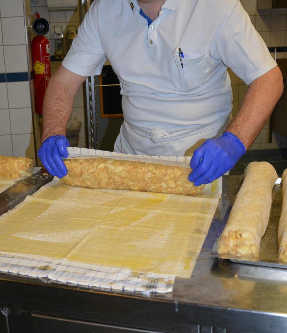 Ein Küchenmitarbeiter rollt einen Apfelstrudel.